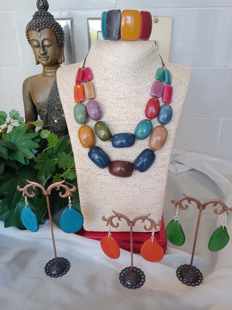 A display of colorful jewelry featuring a beaded necklace on a mannequin, surrounded by decorative earrings on stands, with a Buddha statue in the background.