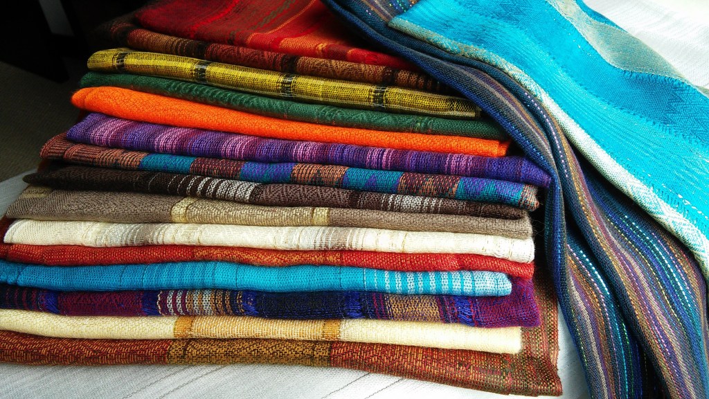 A neatly arranged stack of colorful woven fabrics including shades of blue, orange, red, green, and brown.
